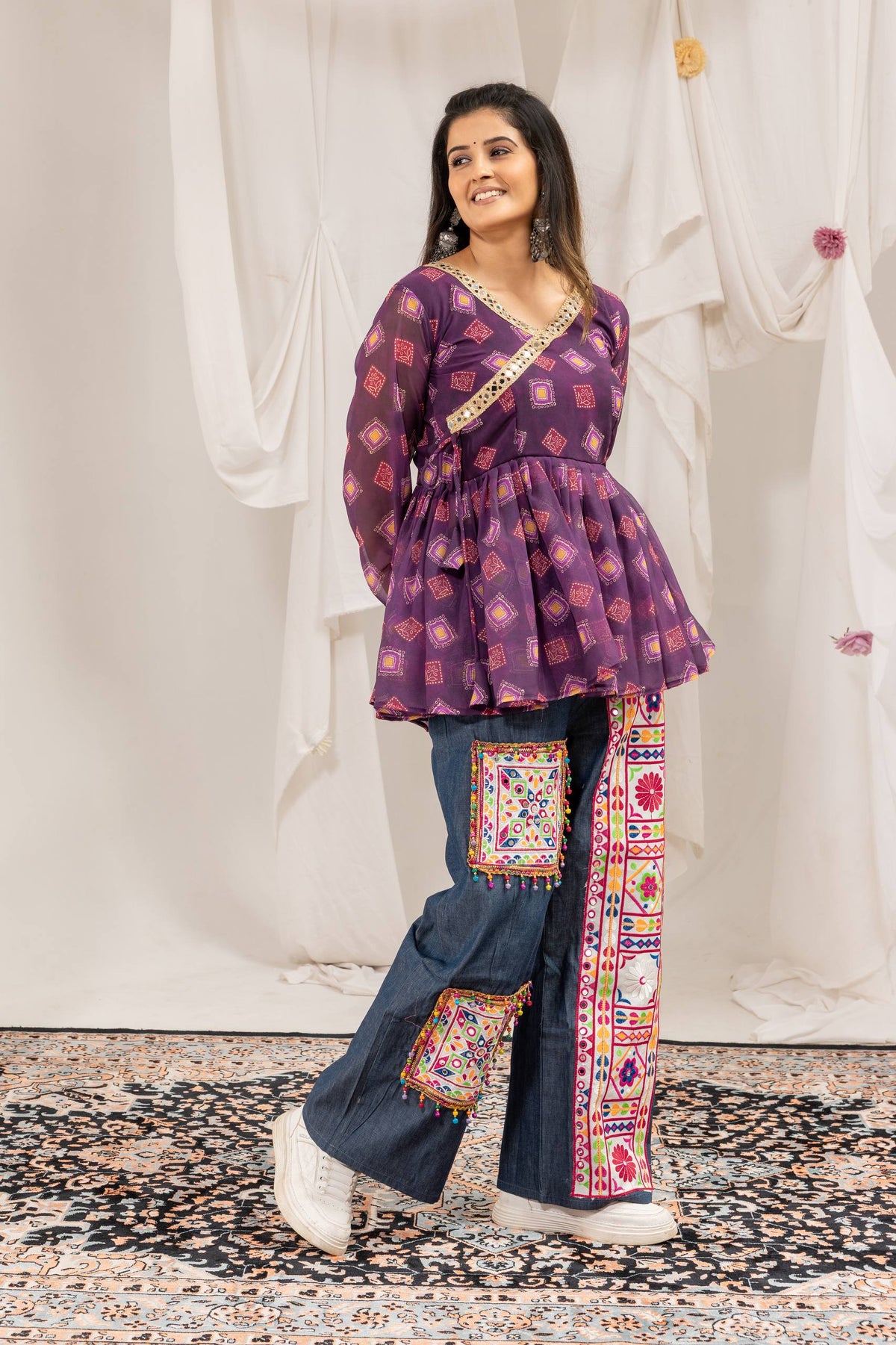 Three-quarter standing pose of model in purple printed flared tunic top paired with embroidered wide-leg jeans