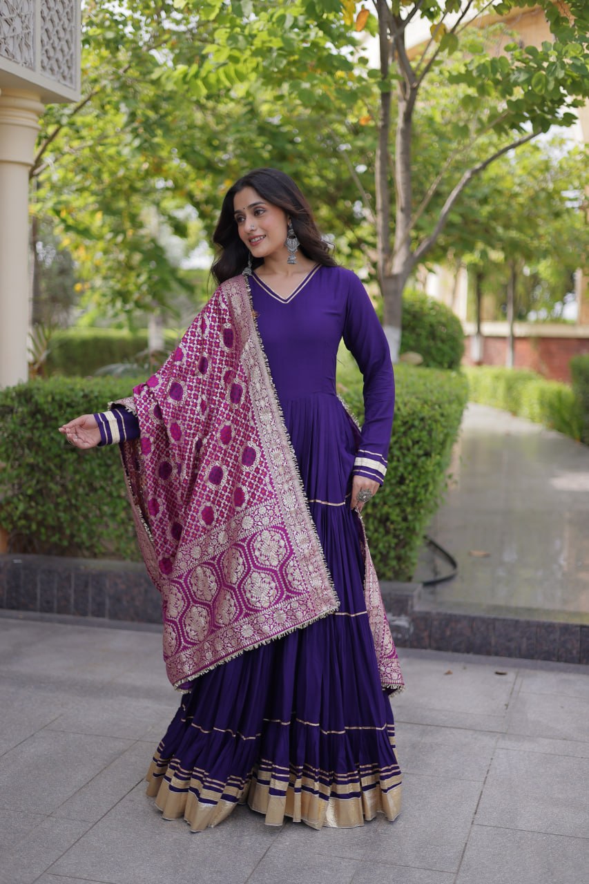 Full-length side-angle view of a model posing outdoors in a royal purple tiered gown complemented by a magenta and gold woven dupatta.