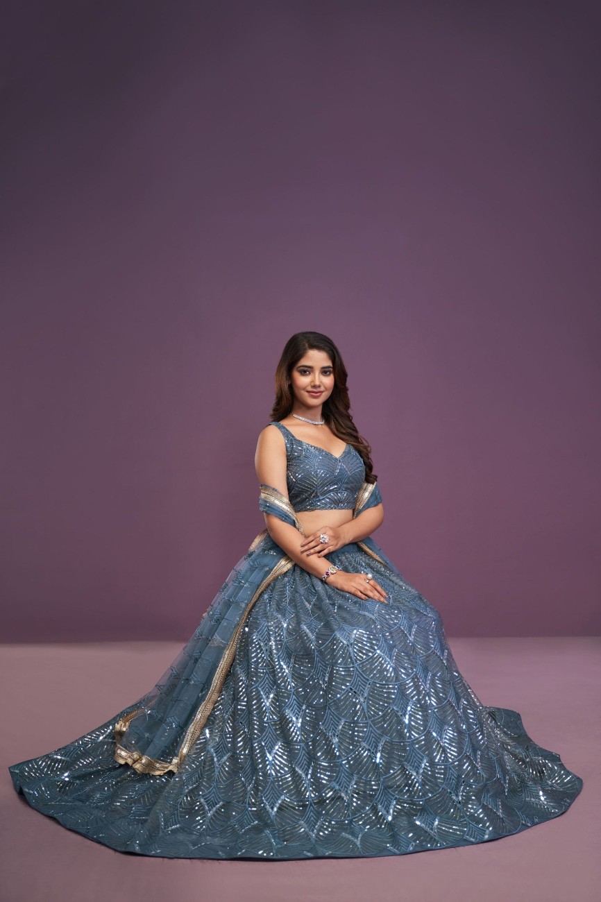 Model seated displaying the full flare of a slate blue lehenga skirt with geometric sequin embroidery