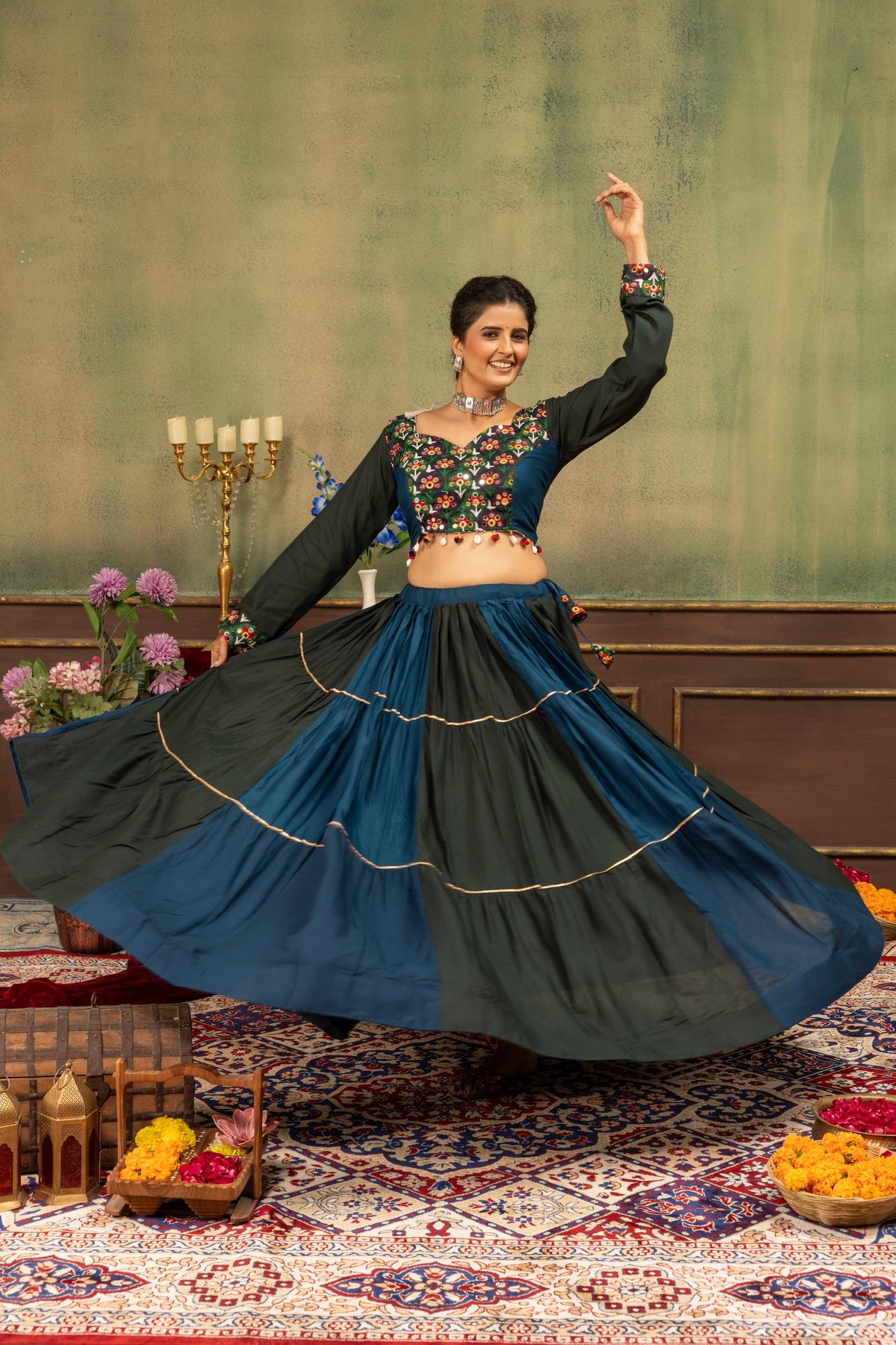 Full-length dancing pose of model displaying the wide circular hem of tiered teal blue and black skirt