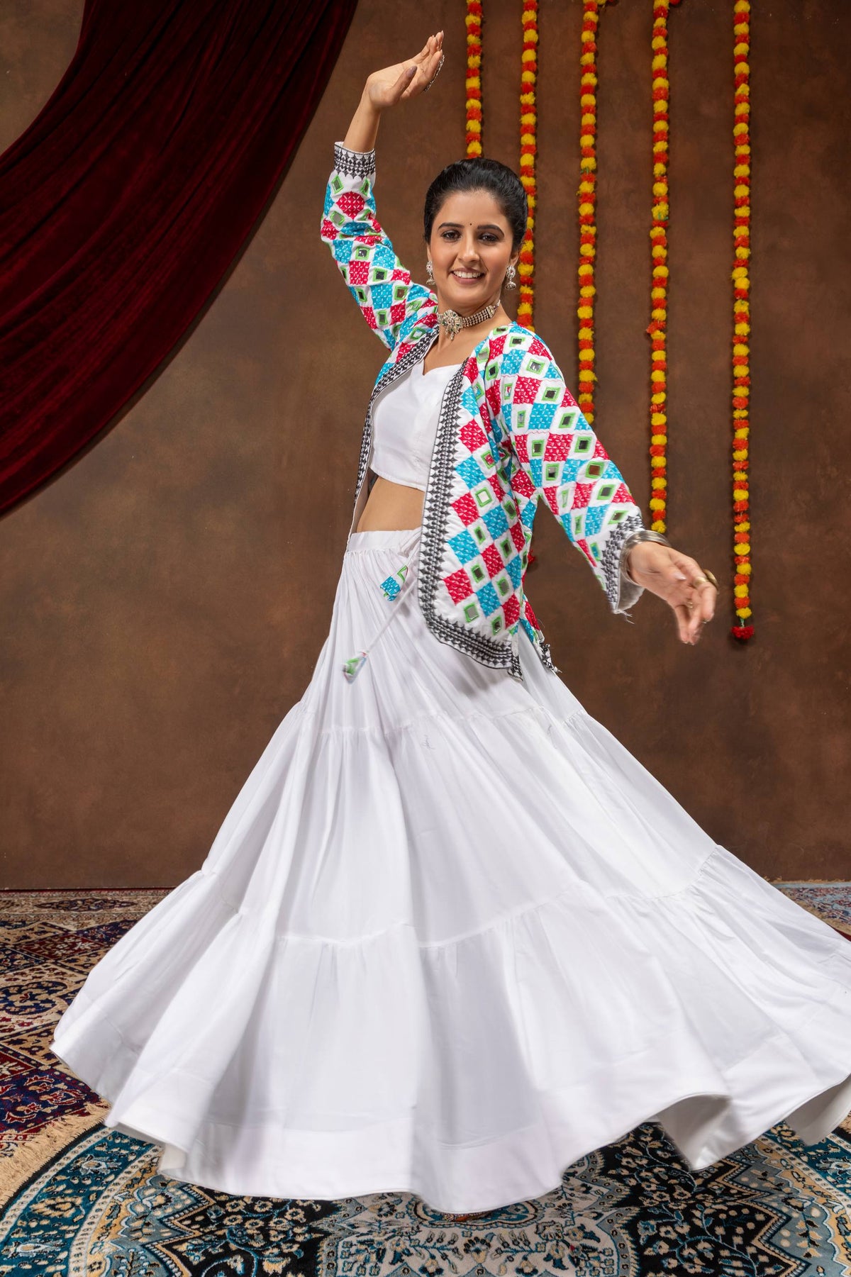 Model in full-spread flared pose holding out white tiered lehenga skirt with arm raised