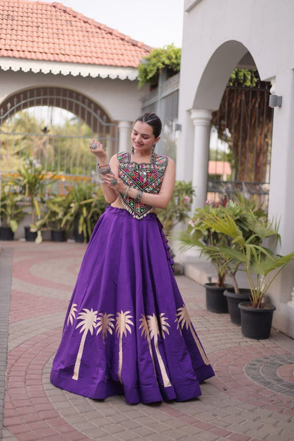 Purple Kutchi Gamthi embroidered lehenga choli with gold coconut gota work, full-length front view while adjusting bangles