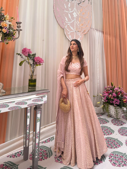 Side-angle full-length shot of a model wearing a baby-pink Chikankari embroidered lehenga with a beaded gold potli bag