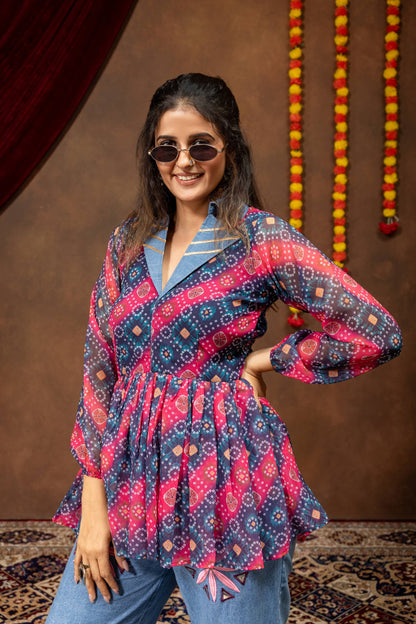 Mid-shot view of model wearing pink and blue printed bandhani peplum top with denim notch lapel collar and sunglasses