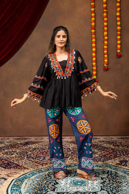 Front standing view of model wearing black flared top with colorful yoke embroidery and wide embroidered denim trousers