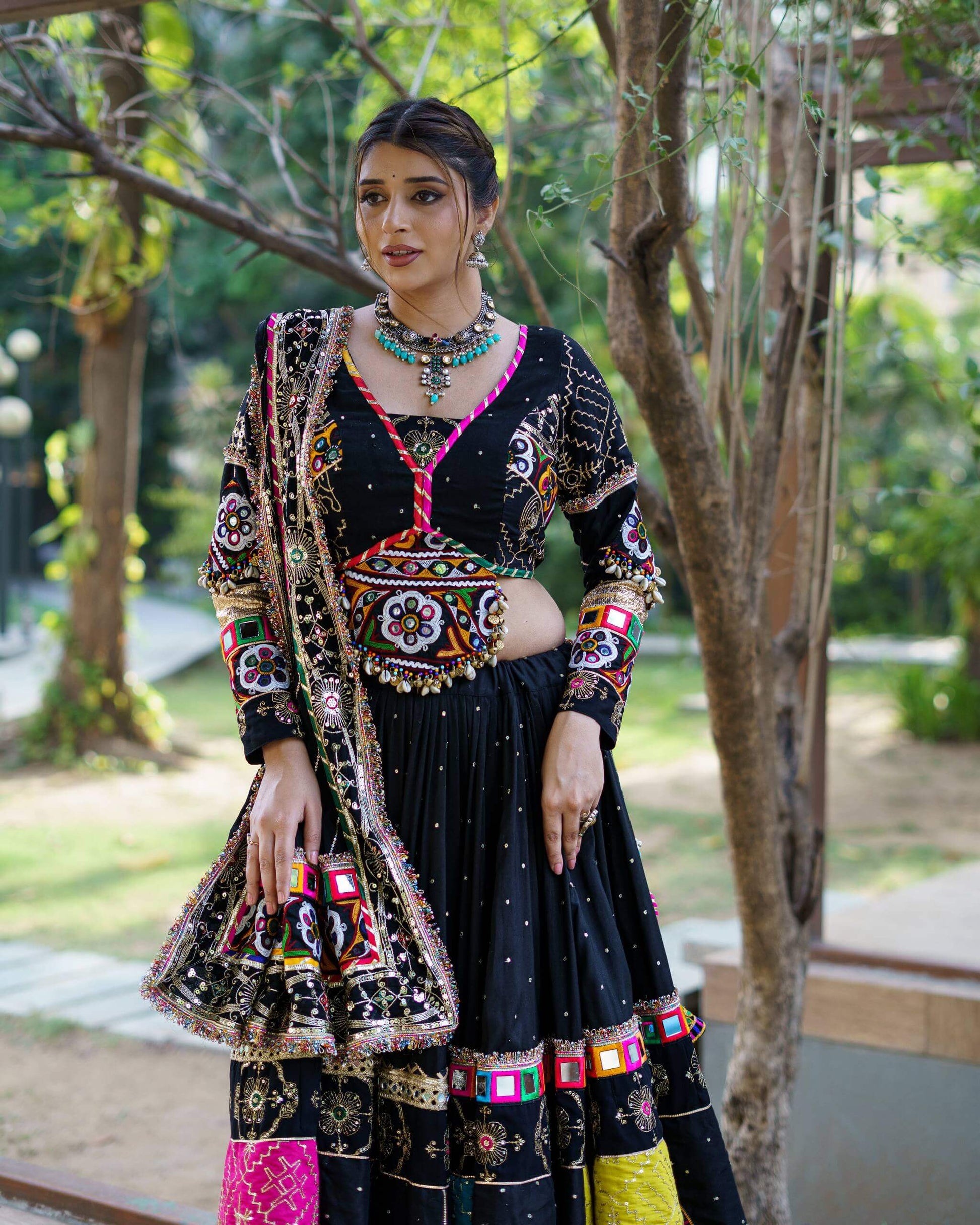 Three-quarter front view of black chaniya choli highlighting the multi-color embroidered patchwork hem and long sleeve blouse