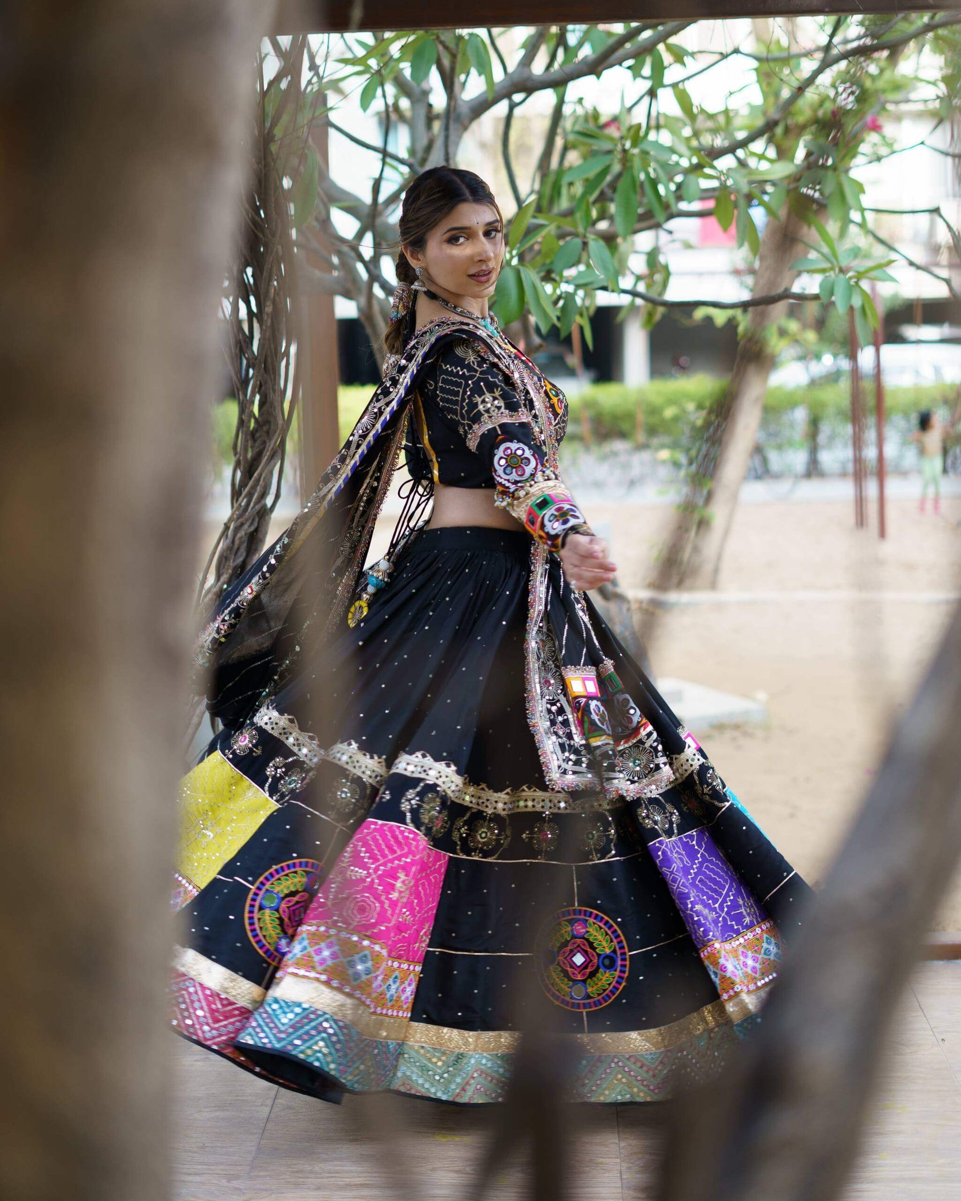 Back view of model twirling in a black chaniya choli showing flare with colorful Kutchi patchwork border and back-tie blouse