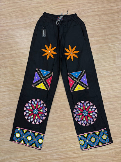 Flat lay view of black palazzo pants featuring embroidered floral, geometric, and mirror-work patchwork designs.