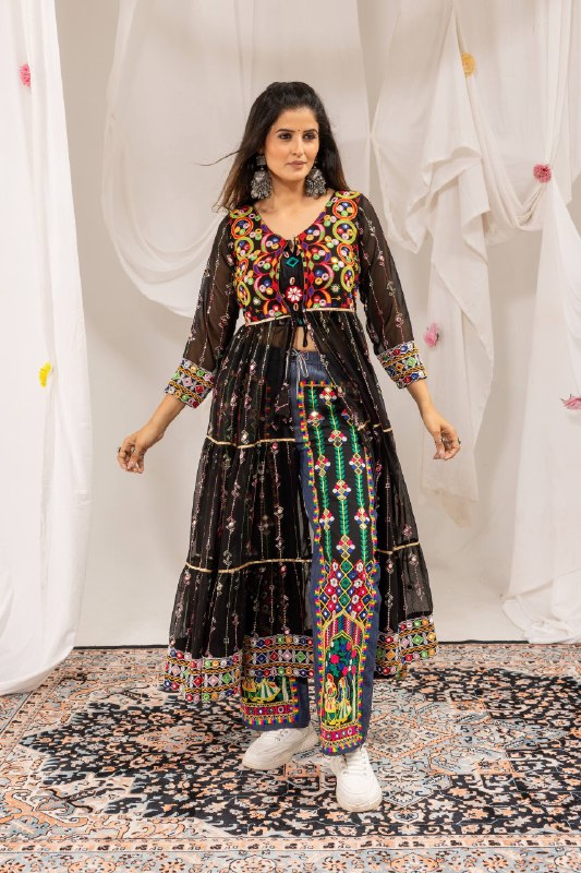 Standing full-length front view of model wearing a black long jacket shrug over blue denim pants with Radha Krishna folk embroidery
