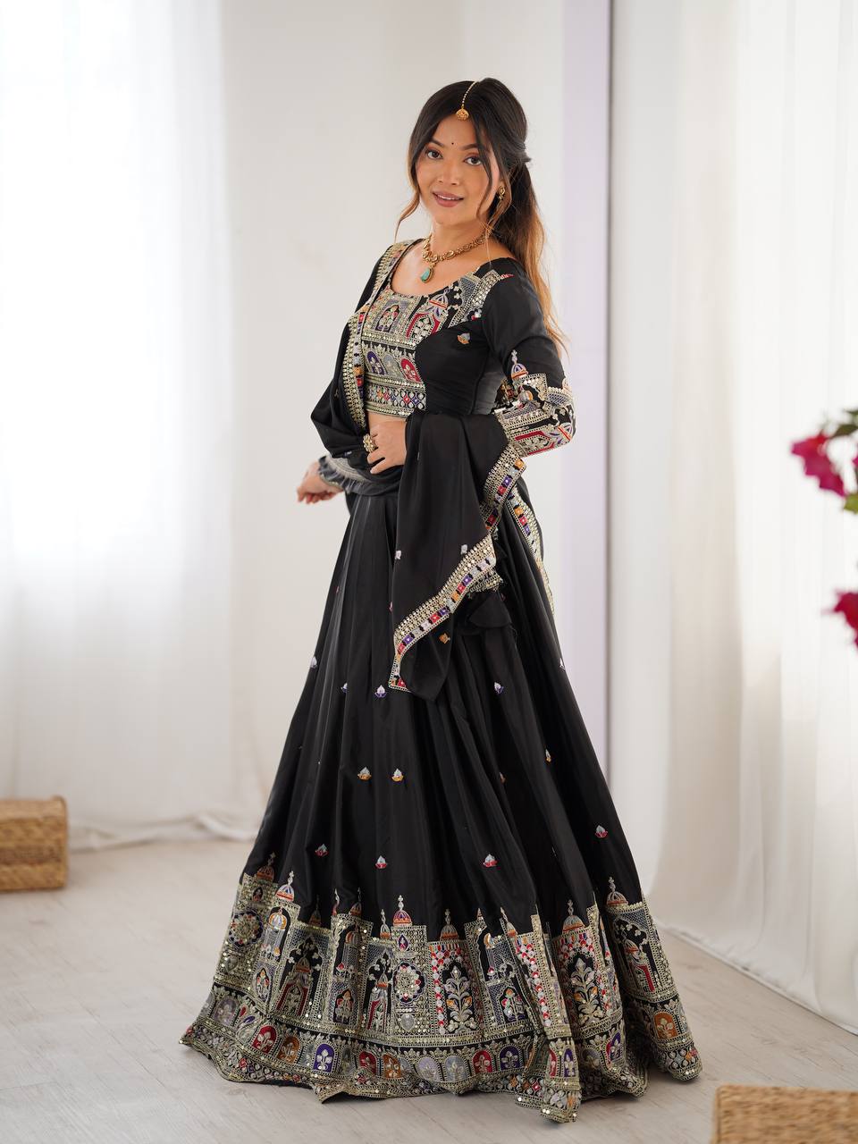 Side pose of model wearing a black pleated lehenga choli with traditional multicolored border work