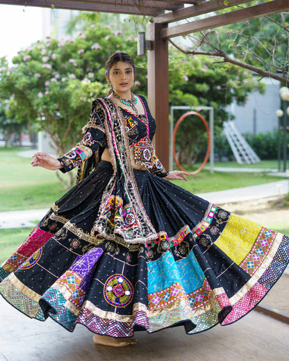 Front view of model holding out the wide flare of a black chaniya choli showing multi-colored mirror embroidered panels