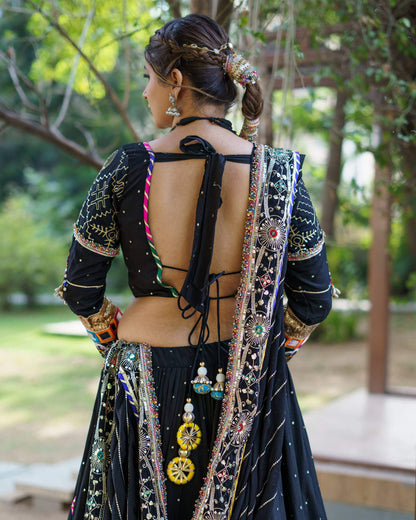 Close-up back view of black choli blouse showing deep open back with tie knot and hanging yellow pompom tassels