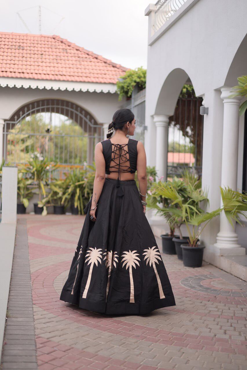 Back view of a black lehenga with beige floral motifs and a lace-up black blouse