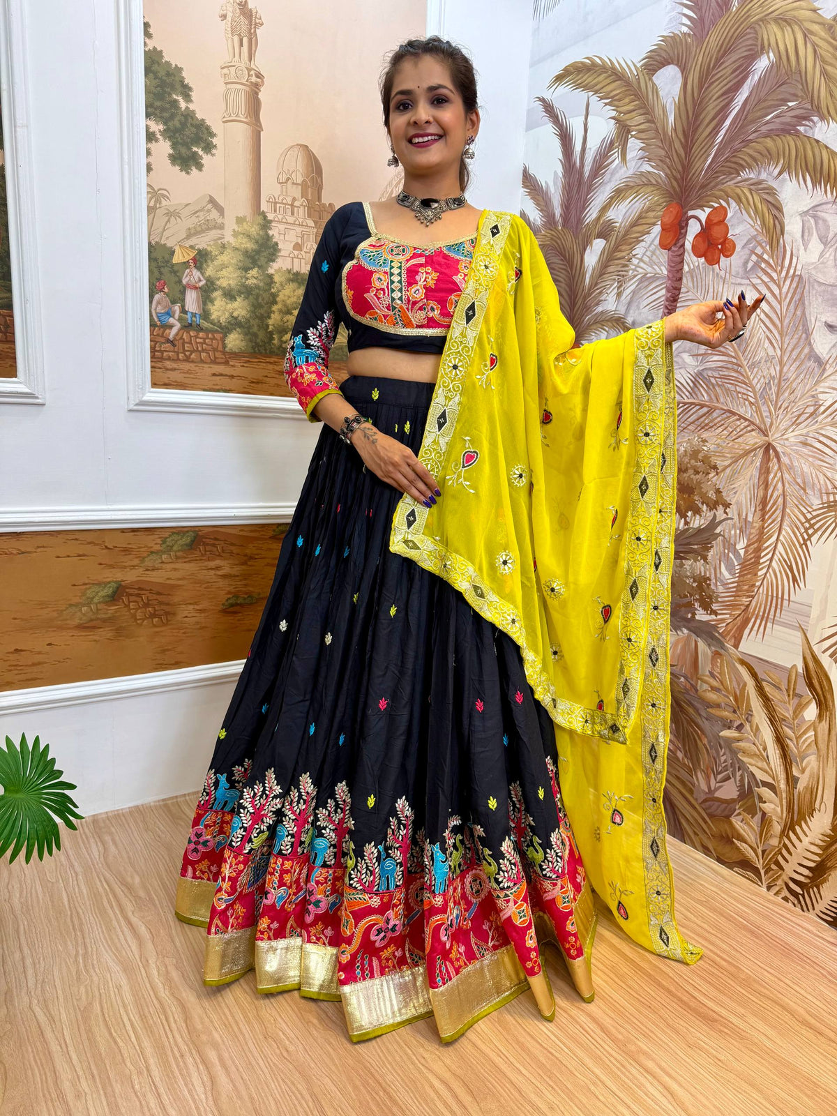 Standing pose of model in a black embroidered lehenga choli holding open a bright yellow dupatta featuring mirror work border