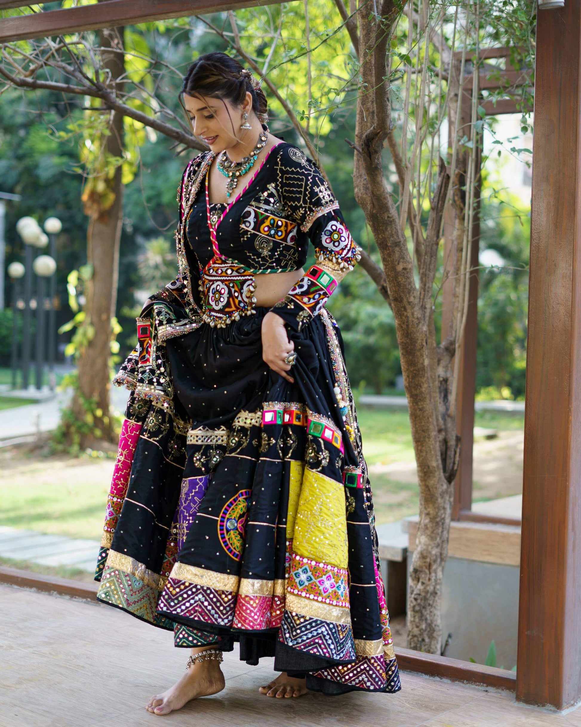 Three-quarter standing view of model wearing a black Navratri lehenga with yellow and pink border patches and embroidered long-sleeve blouse