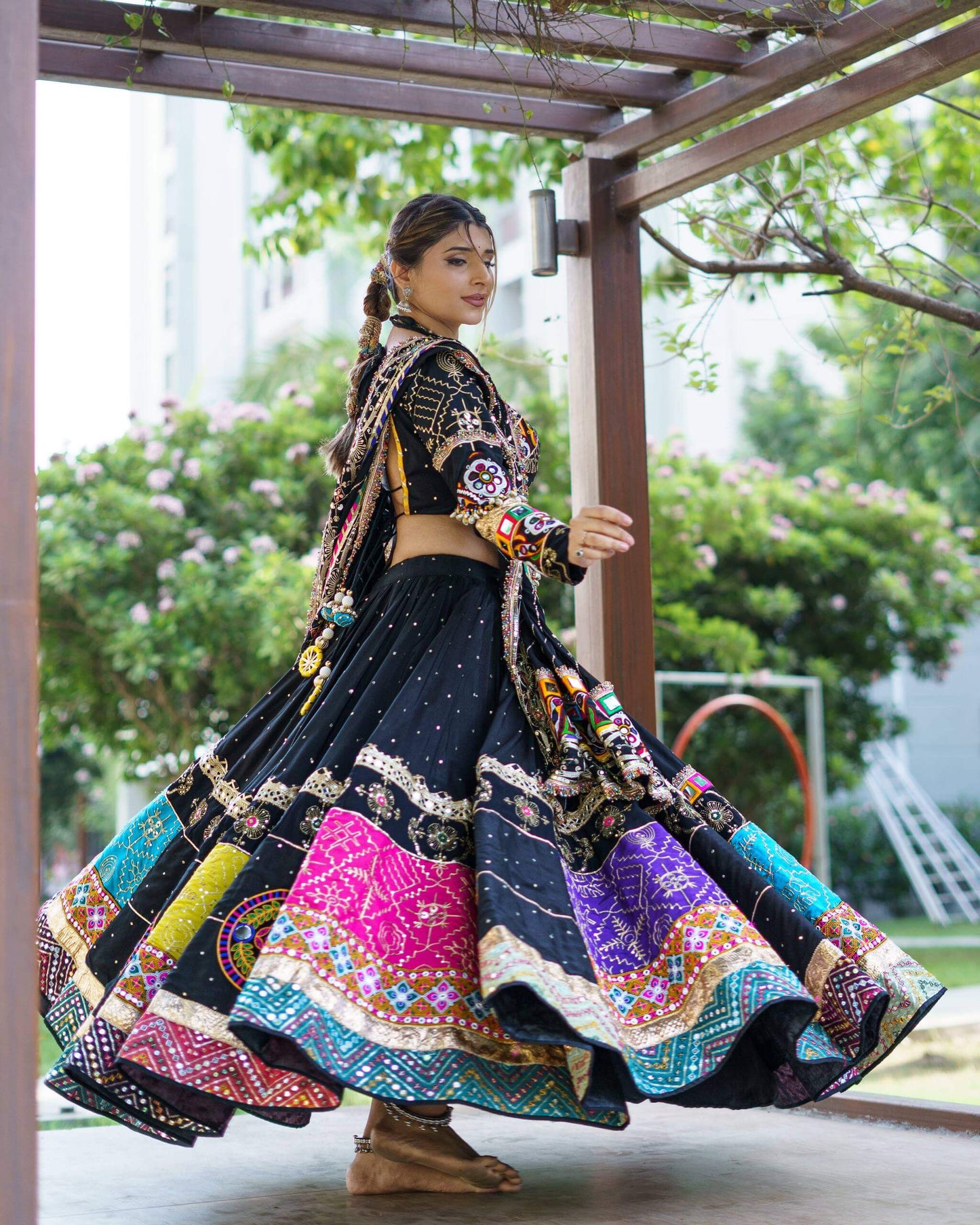 Side twirling pose showcasing the voluminous flare of a black Navratri lehenga with vibrant embroidered border bands