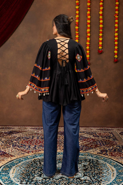 Back view of model wearing black peplum top featuring criss-cross back tie-up strings and wide-leg blue jeans