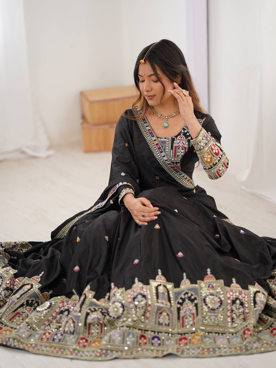 Seated view of model showing detailed border embroidery and embellishments on a black flared lehenga