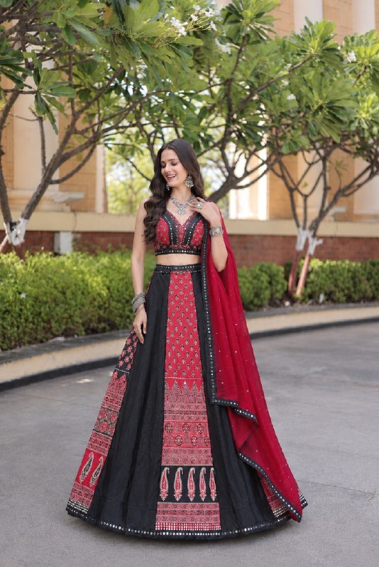 Standing full-length front view of a model wearing a paneled black and red printed lehenga with mirror-lace borders and matching sleeveless choli.