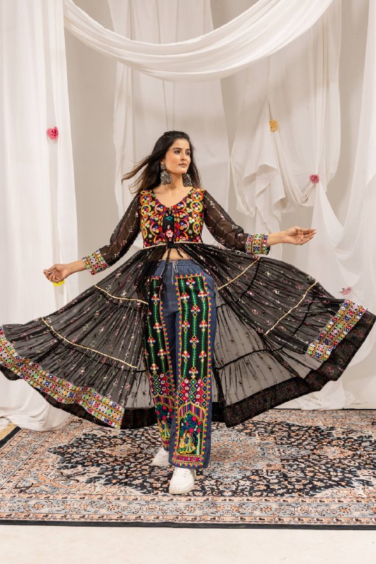 Model in dynamic full-length pose spreading a black sheer tiered long shrug over embroidered blue denim pants
