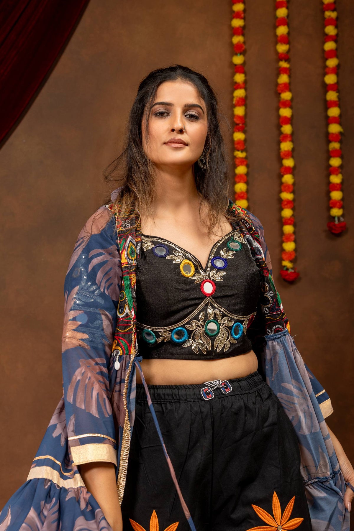 Front mid-shot view of a black sweetheart neckline crop top with mirror work accents worn under a blue open jacket shrug.