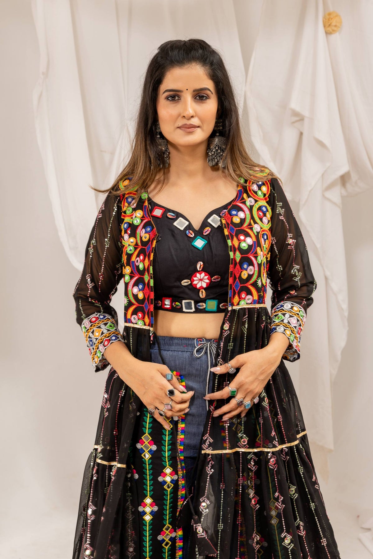 Mid-shot view of a model in a black sweetheart crop top embellished with shells, under a colorful mirror-work shrug