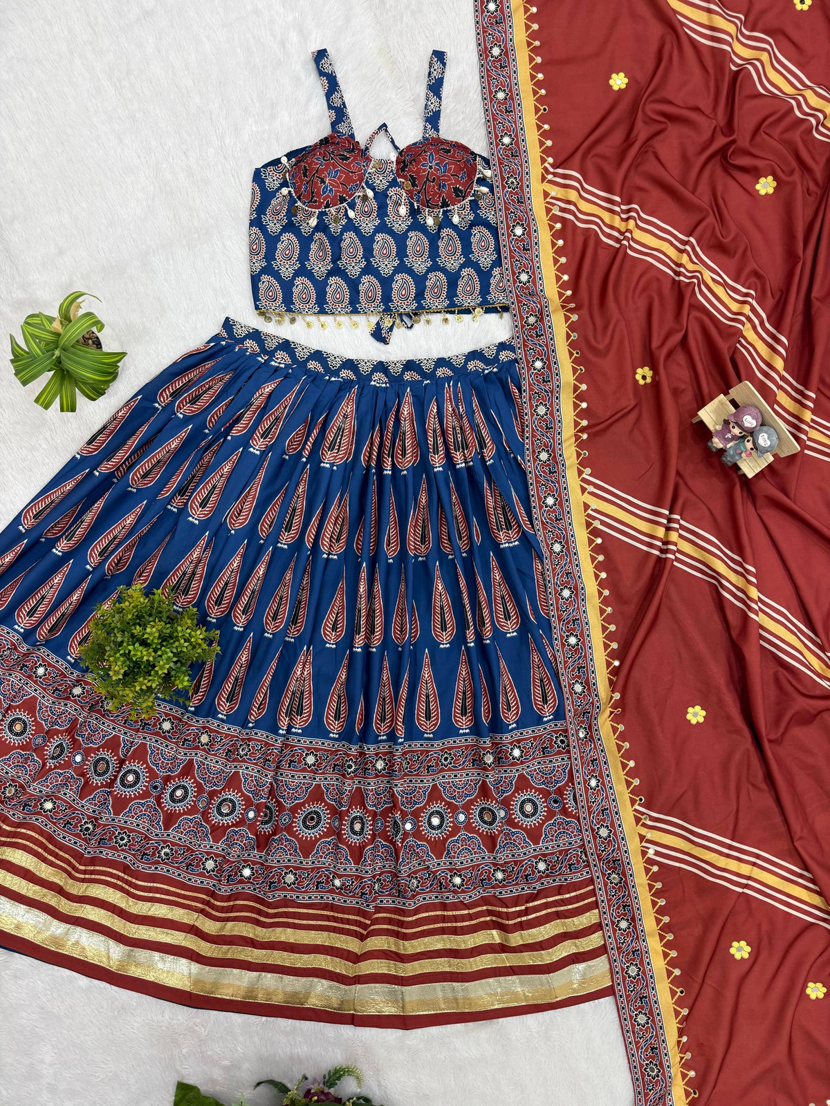 Flat lay view of blue Ajrakh print lehenga choli set with cowrie shell tassels and maroon dupatta