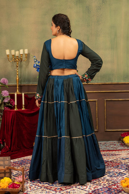 Back view of model wearing deep U-back blue blouse and dark tiered panelled lehenga skirt with gold gota piping