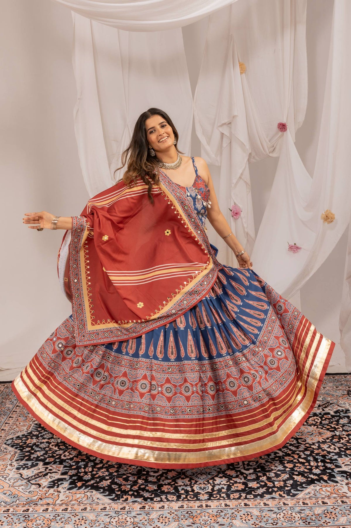 Model spreading flared blue printed lehenga skirt finished with maroon band and gold gota patti hem