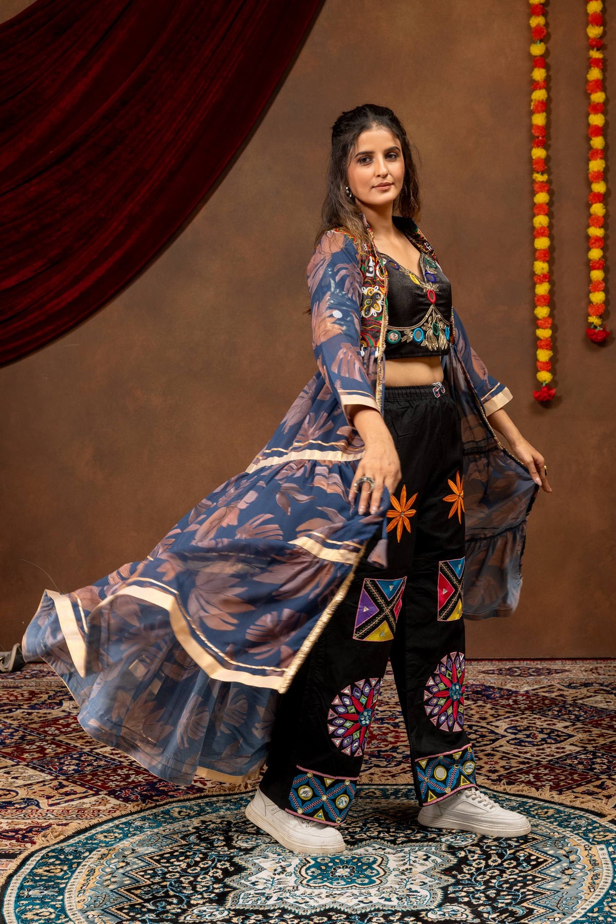 Three-quarter view of a model in a voluminous flared blue printed shrug jacket and black embroidered wide-leg palazzo pants.