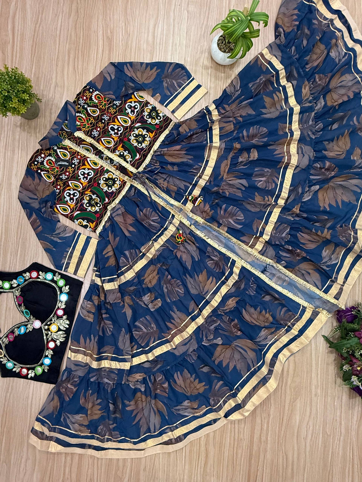 Flat lay view of the blue printed tiered shrug with gold border lace paired with a black mirror-work crop top.