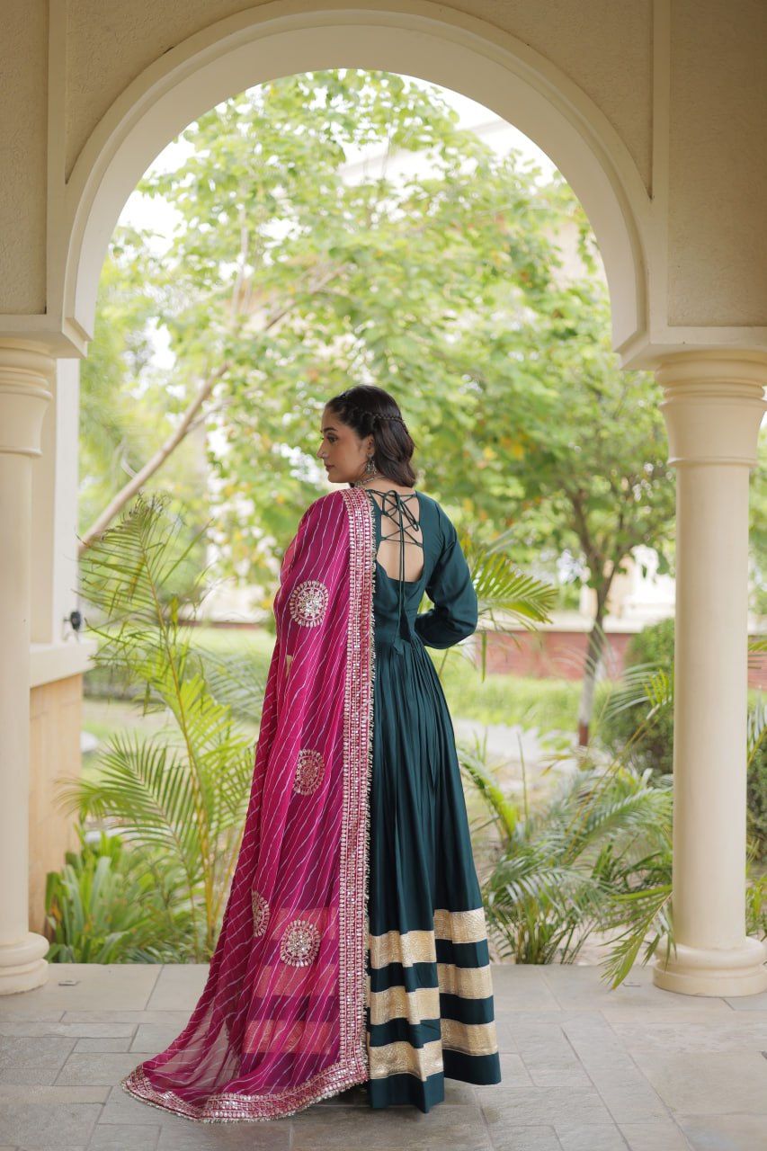 Full-length back view of a dark green flared anarkali gown showing a cut-out back with criss-cross tie-up dori and draped pink dupatta.