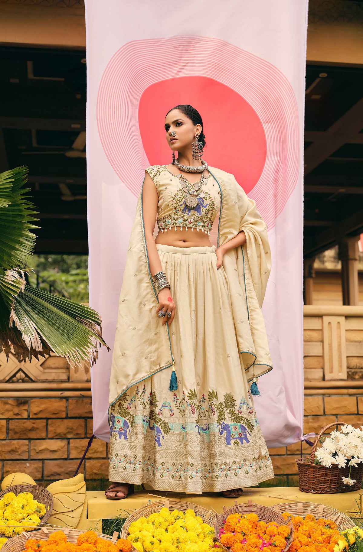Full-length pose of model wearing a pleated cream lehenga and matching dupatta with teal edge piping