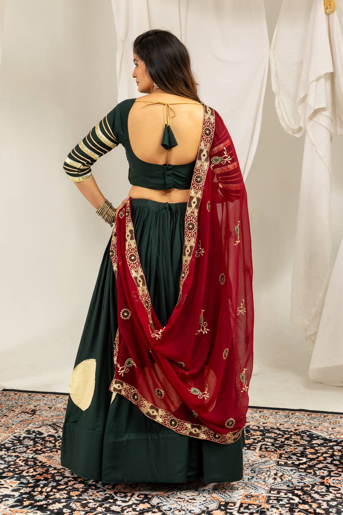 Back view of a model highlighting the deep scoop back neckline and tie-up tassels on a dark green blouse.