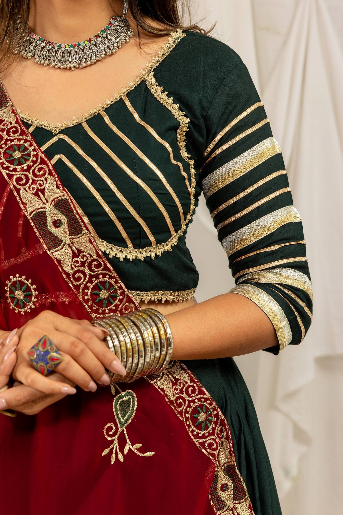 Close-up view of the dark green blouse showing diagonal and horizontal gold striped embroidery with lace border trim.