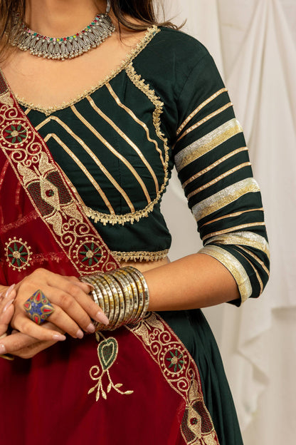 Close-up view of the dark green blouse showing diagonal and horizontal gold striped embroidery with lace border trim.