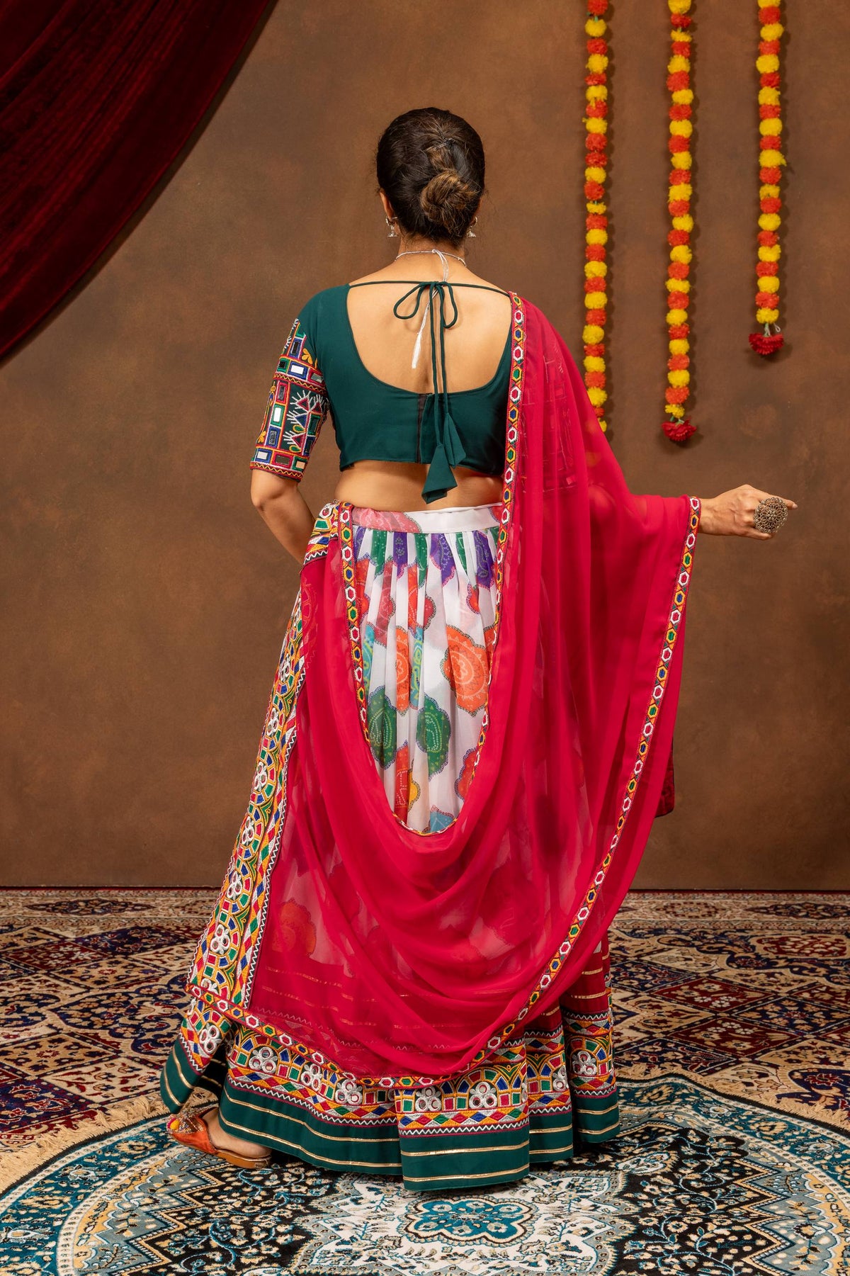 Back view of model wearing dark green blouse with tie-up dori and draped pink mirror work dupatta