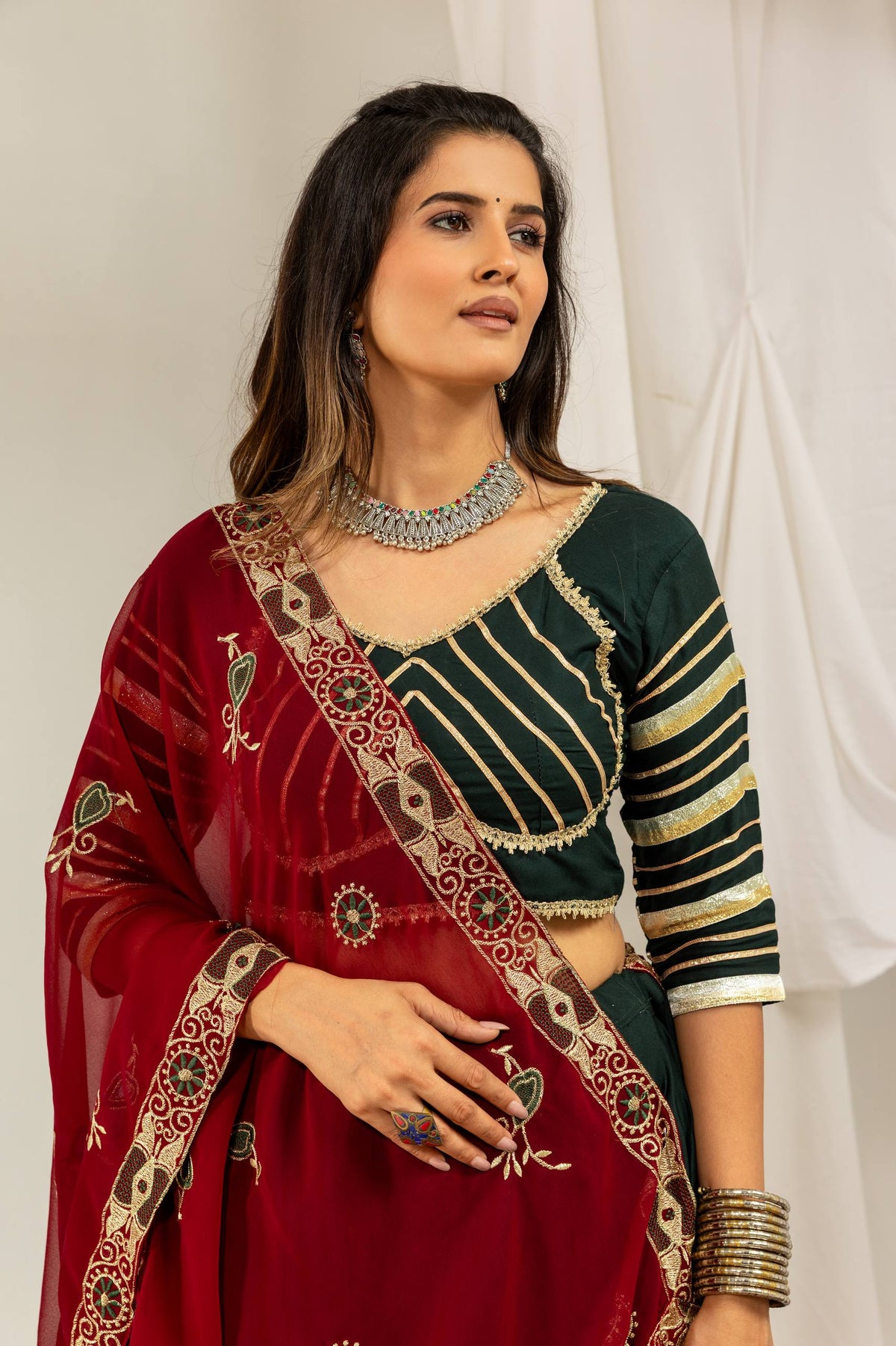 Mid-shot view of a dark green choli with gold striped sleeves paired with a draped maroon embroidered dupatta.