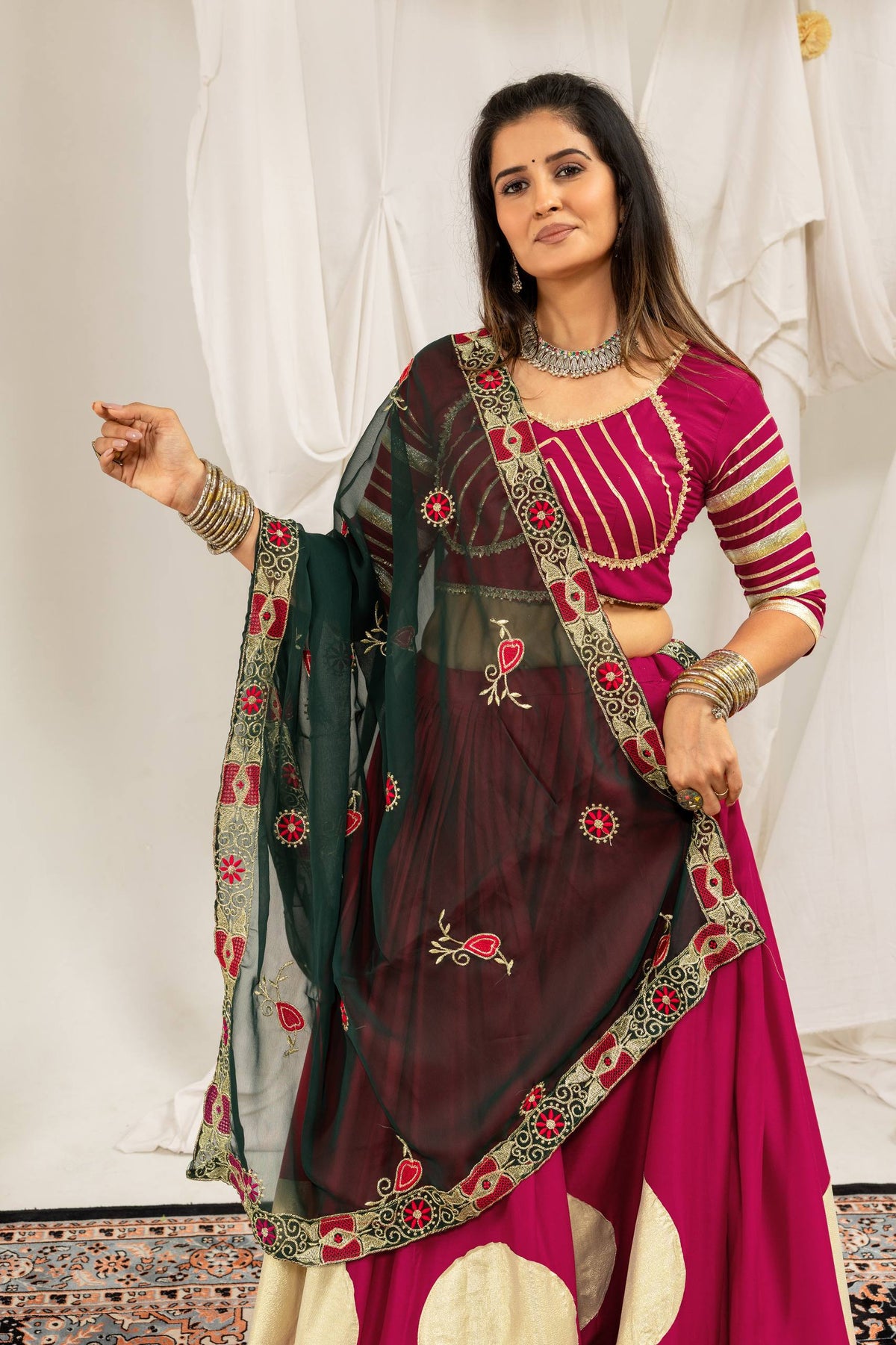 Three-quarter front view highlighting a dark green embroidered dupatta draped over a magenta lehenga choli set.