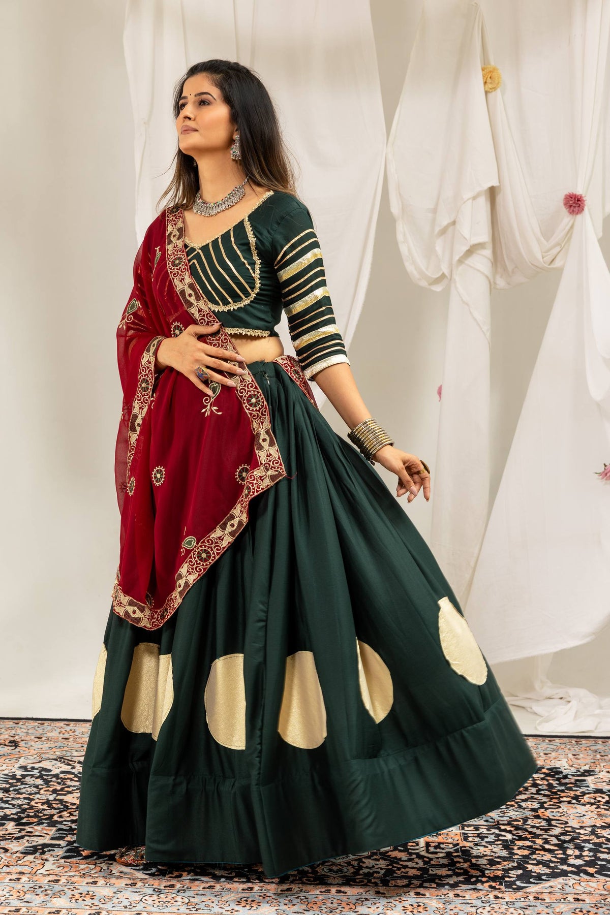 Three-quarter standing pose of a model dressed in a dark green flared lehenga skirt and elbow-sleeve striped blouse.