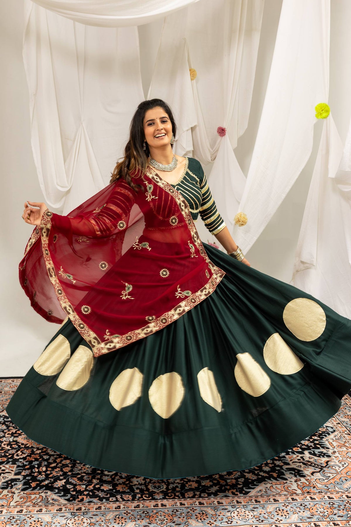 Action view showing the wide flare of a dark green lehenga skirt accented with gold circle motifs and a maroon dupatta.