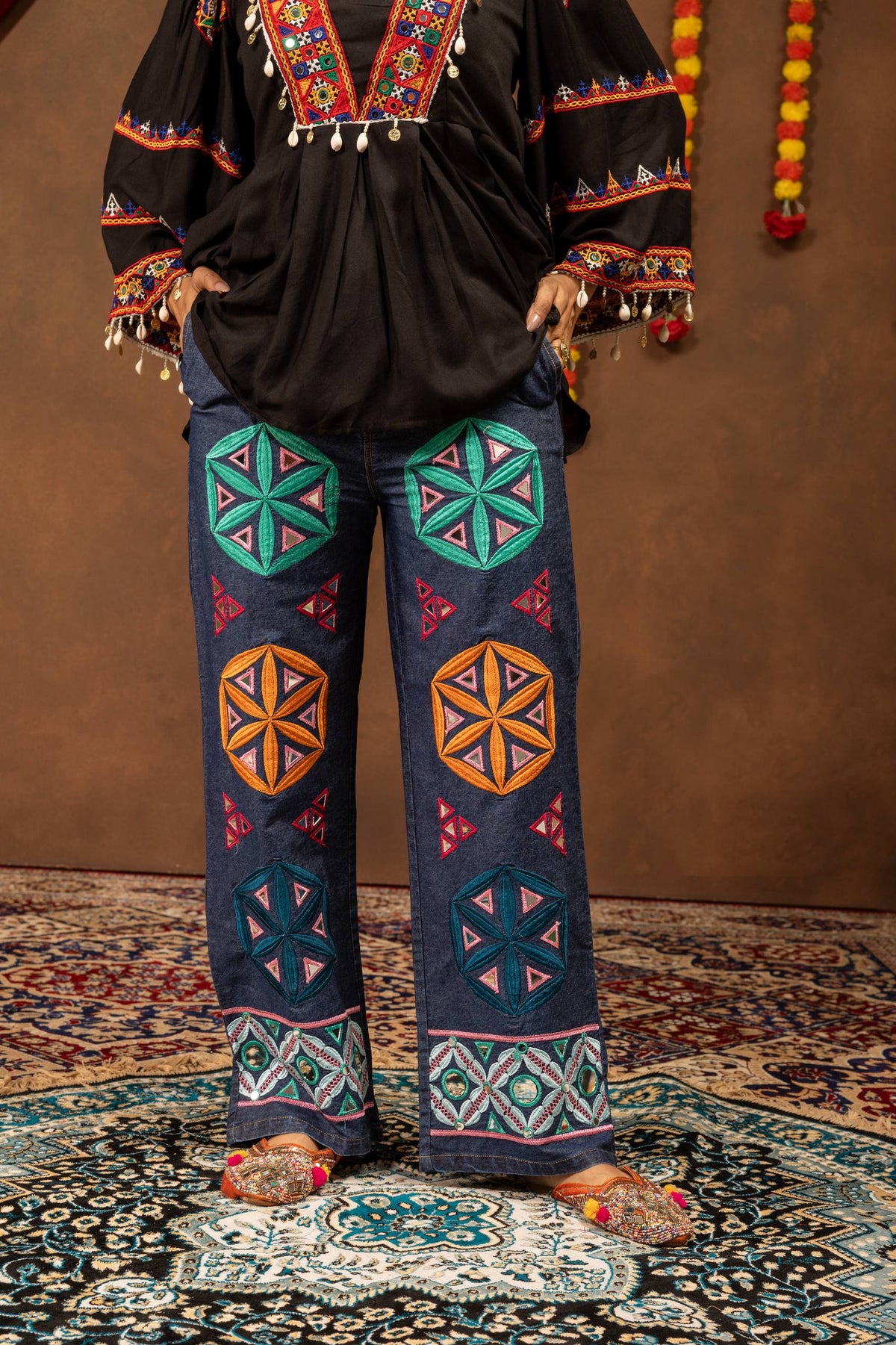 Close-up front view of wide-leg blue jeans adorned with colorful geometric floral patches and mirror work embroidery