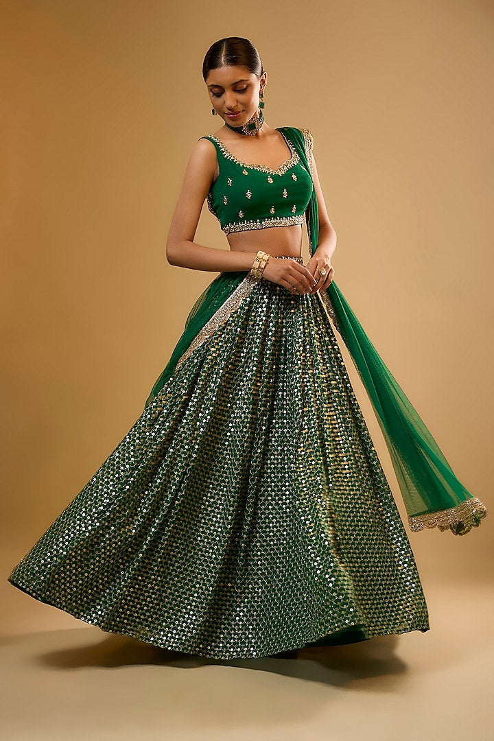 Side-angle full-length shot showcasing the wide flare of an emerald green mirror-work lehenga paired with a sheer scalloped dupatta.