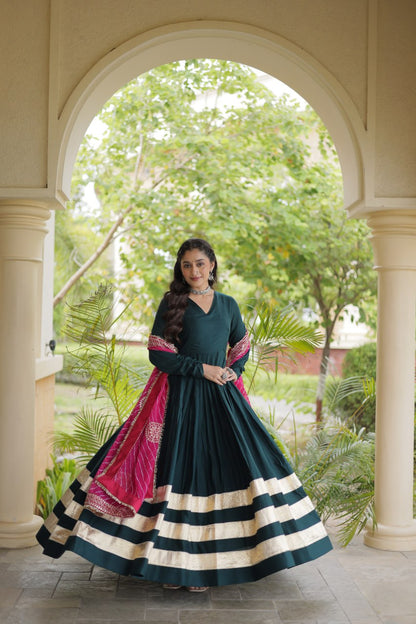 Full-length shot capturing the wide flare of an emerald green tiered gown with bold gold border stripes and draped pink dupatta.