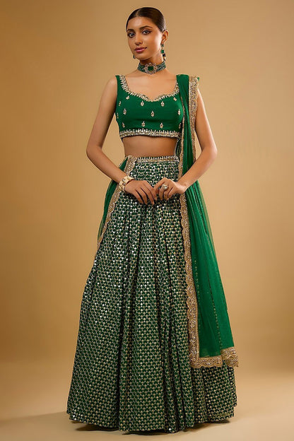 Standing full-length front view of a model wearing an emerald green lehenga choli with allover mirror embellishments and matching border dupatta.