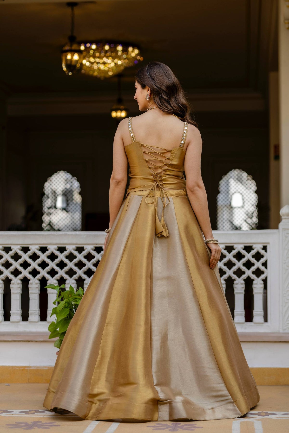 Full-length back view of model wearing a gold flared lehenga and sleeveless corset blouse with lace-up dori tie-up back