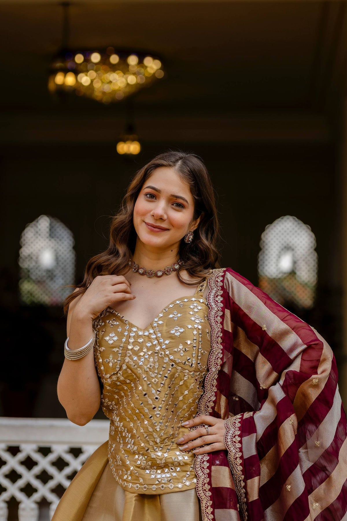 Portrait view of model wearing a sweetheart neck gold mirror embellished blouse with maroon and gold striped dupatta