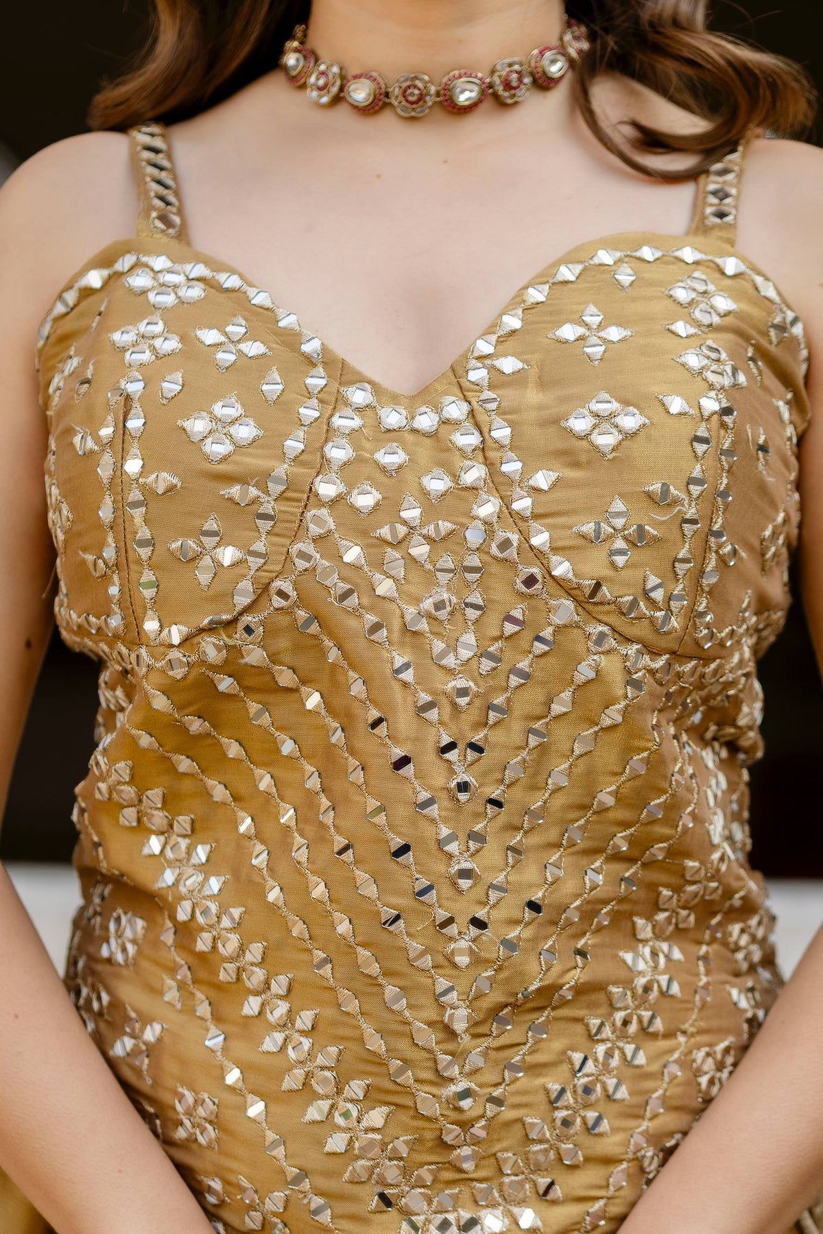 Close-up front view of gold sleeveless corset blouse with sweetheart neckline and geometric mirror embroidery