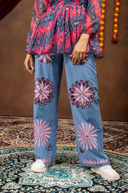 Lower body close-up view of wide-leg light blue denim jeans embellished with pink floral and circular mirror embroidery