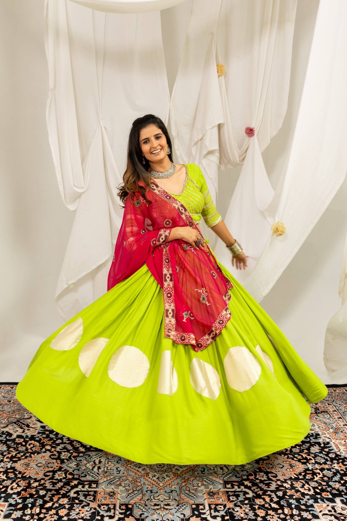 Wide circular flare action display of a lime green lehenga skirt accented with gold circle motifs and a contrasting hot pink dupatta.